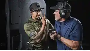 Man getting the attention of another man holding a handgun at an indoor shooting range.